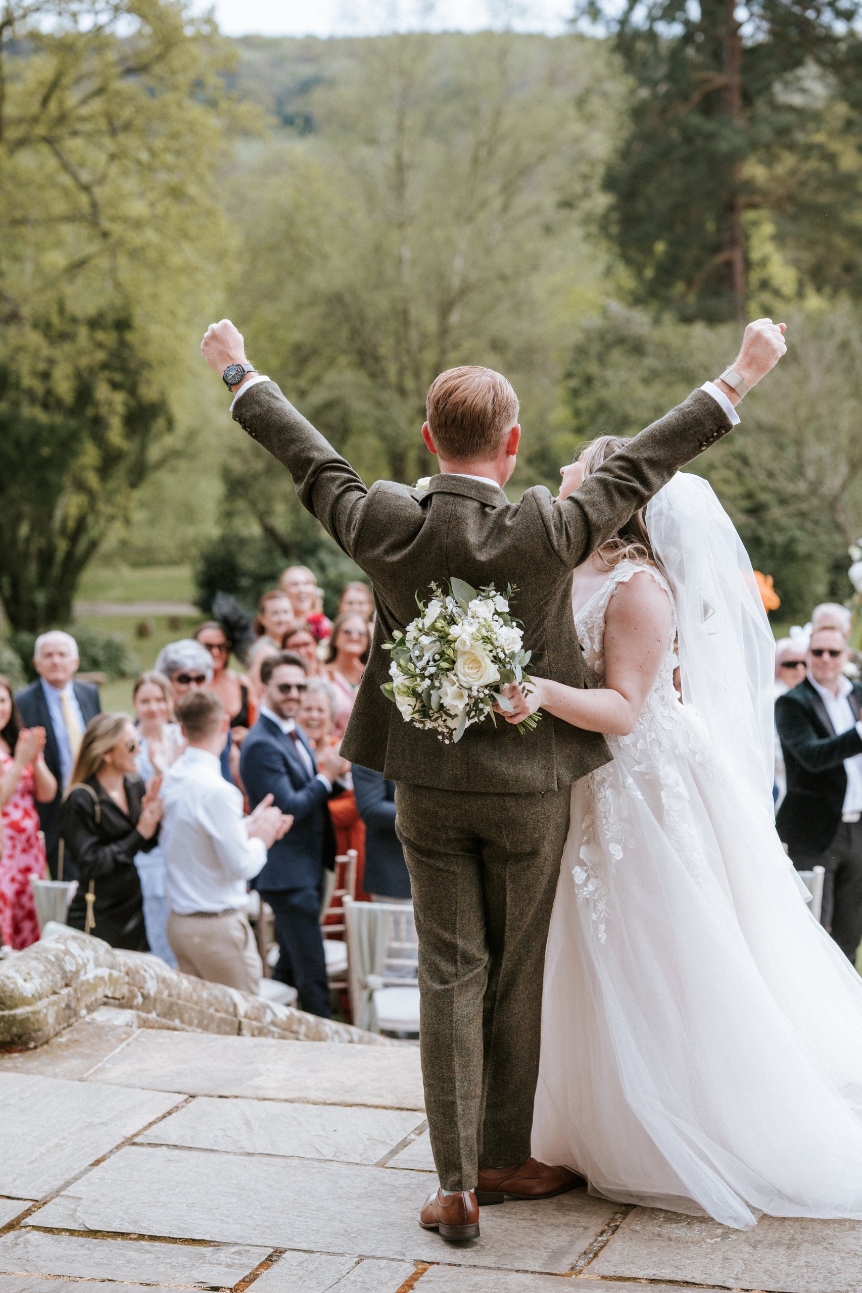 Newlyweds celebrating with arms raised as guests applaud